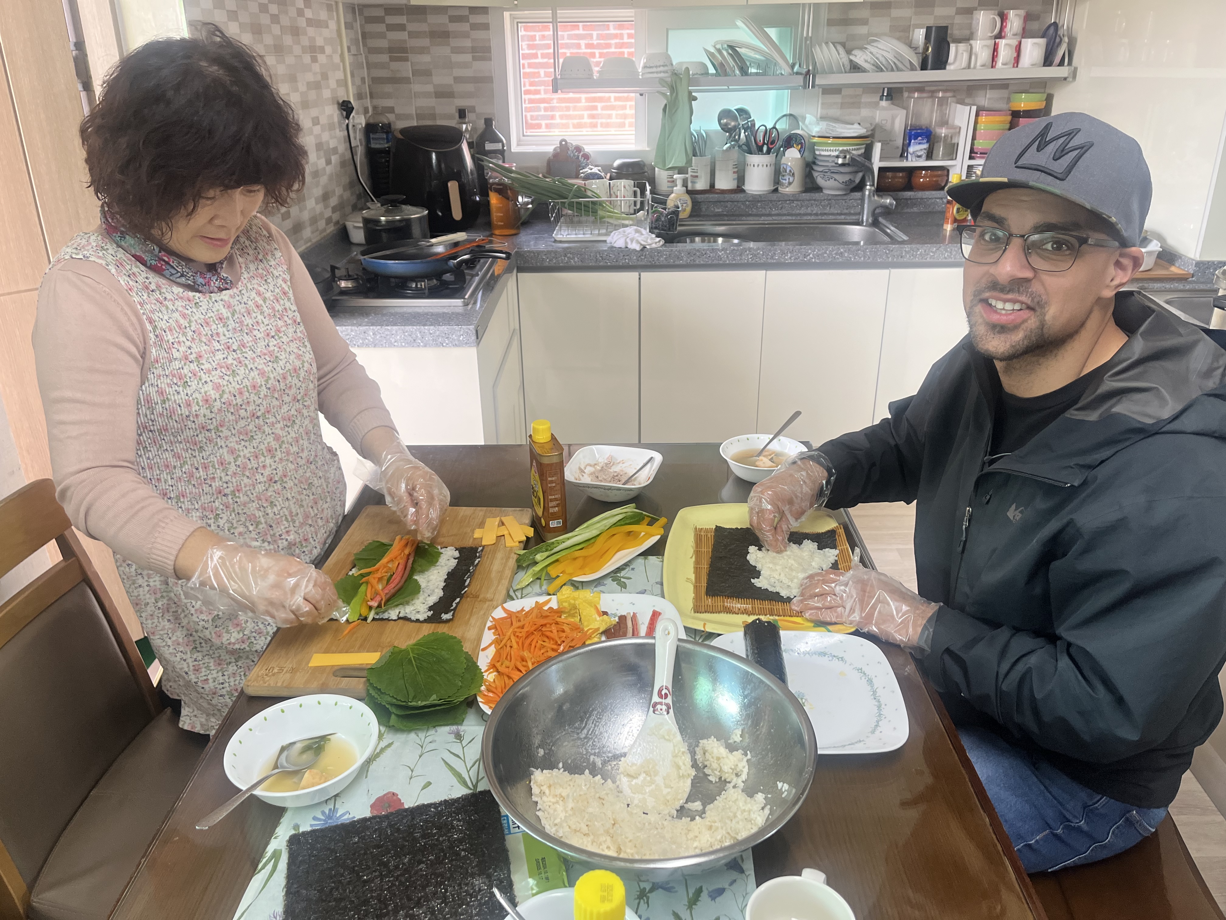 Mom teaching a guest how to make gimbap in the family kitchen